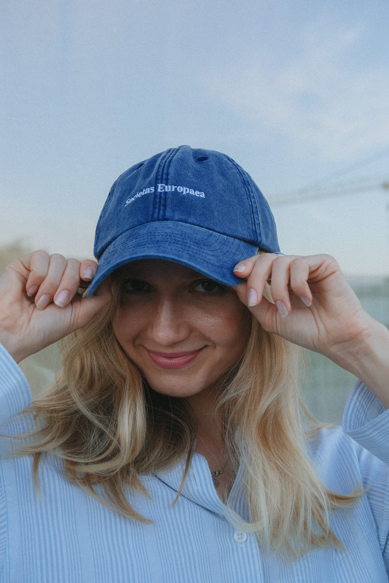 A smiling teammate holding the brim of her blue cap.