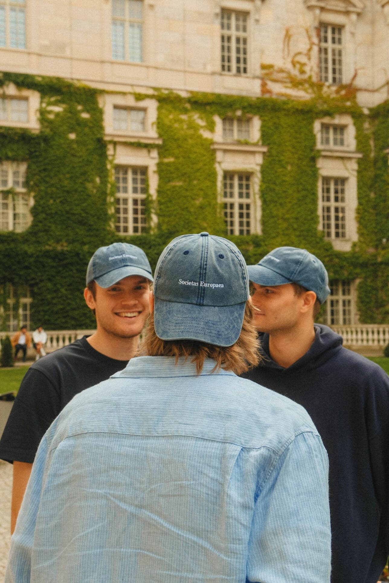 Three teammates in blue caps chatting in a courtyard.