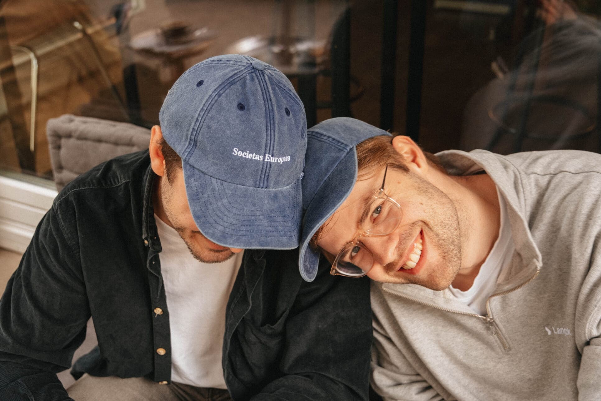 Two friends leaning together in matching blue caps.