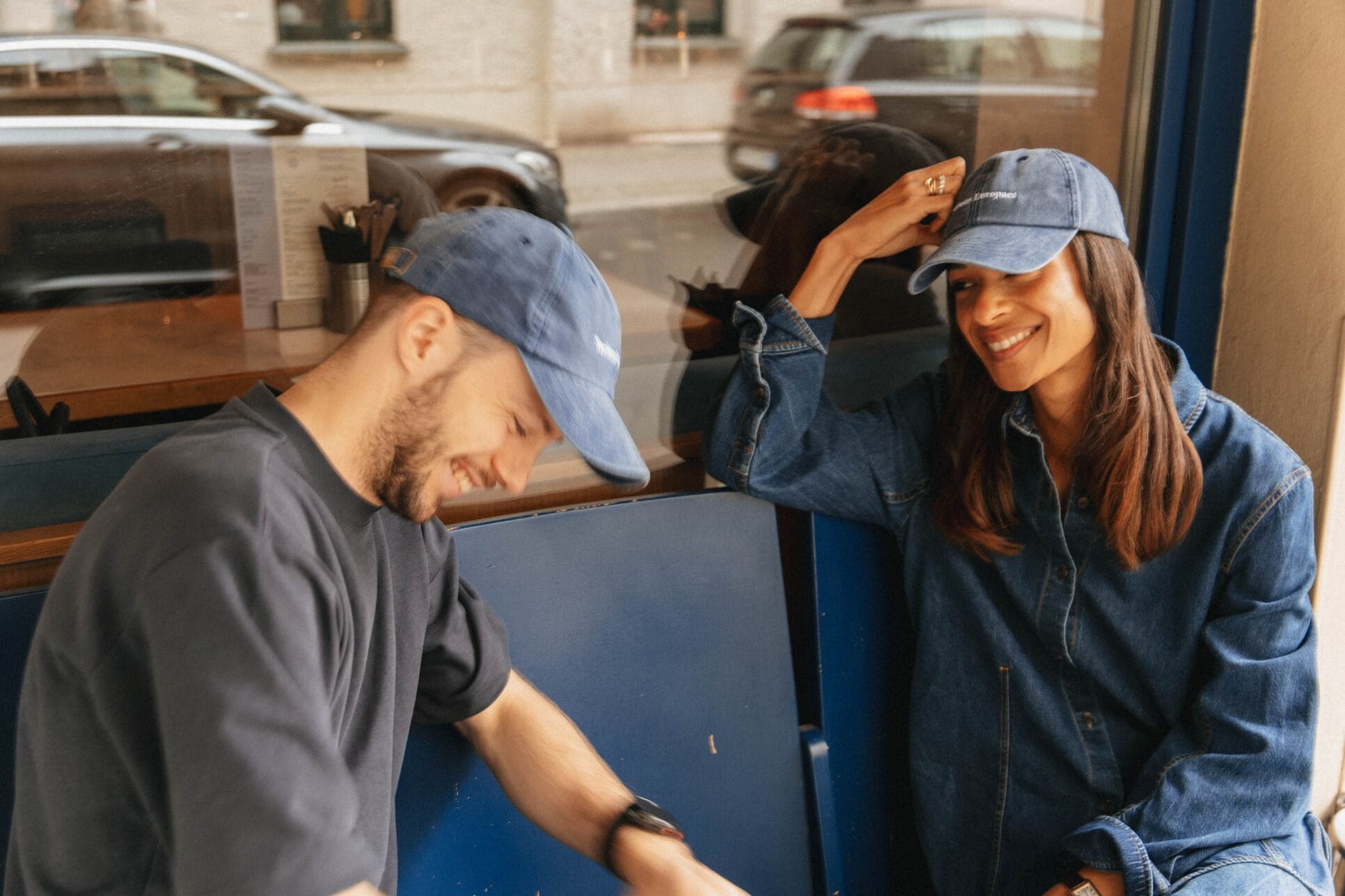 Two teammates in blue caps laughing together outside a café.