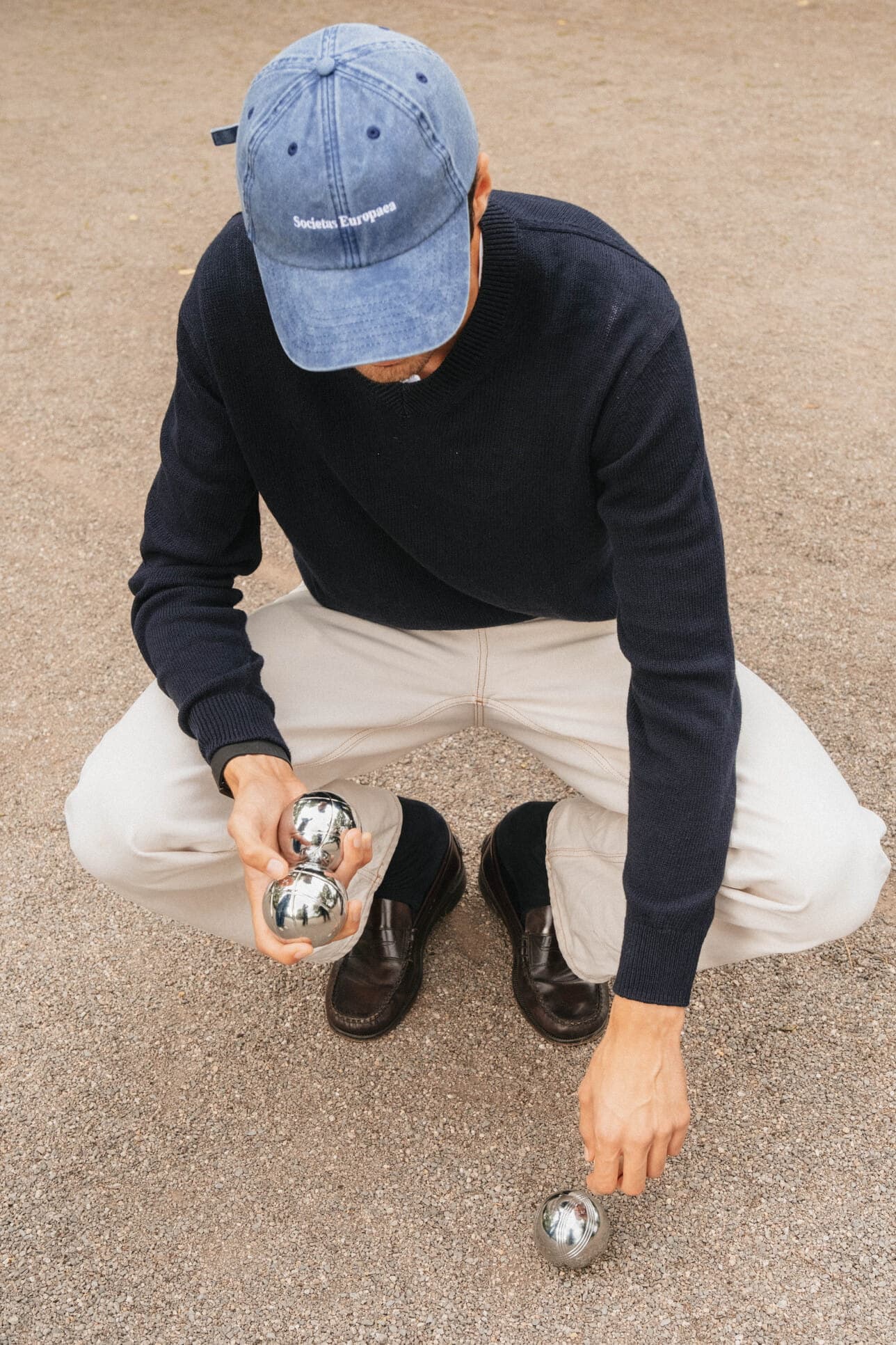 A teammate in a blue cap playing pétanque.