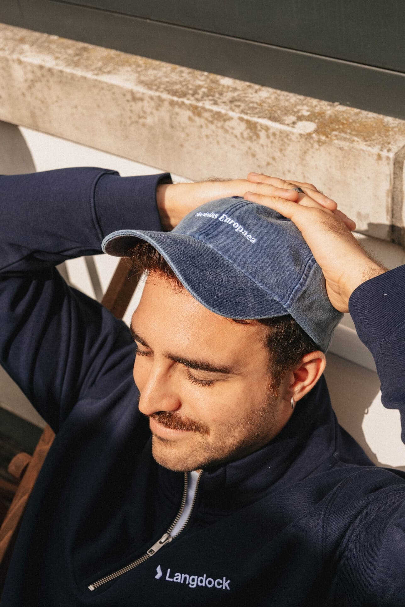 A teammate relaxing with a hand on his blue cap.