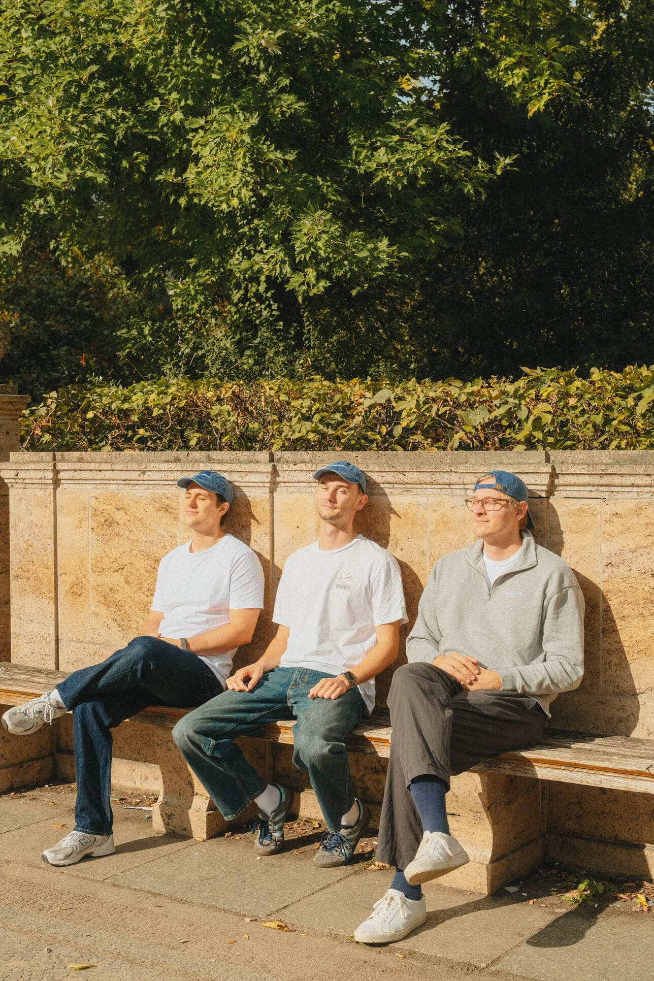 Three teammates in blue caps relaxing on a sunny bench.